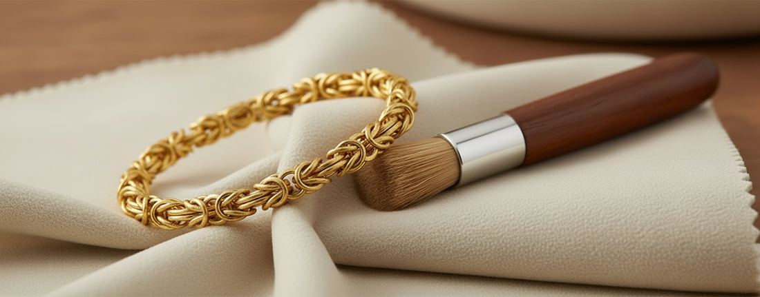 Handmade gold Byzantine bracelet resting on a soft cleaning cloth with a wooden-handled brush